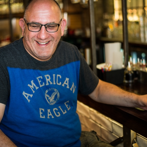 Gary mazin sitting at a bar, wearing a blue top and laughing
