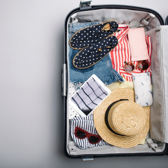 An open trolley case with a hat, sunglasses, striped red top, jeans and polka dot shoes
