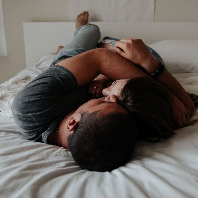 Sex that's out of sync - A man and woman cuddling on a bed, the bedding is white and the image is taken from their head looking down their clothed bodies.
